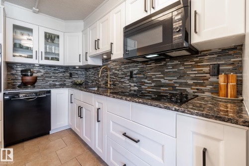 Modern kitchen featuring white shaker cabinetry, dark countertops, a mosaic tile backsplash, stainless steel appliances, and tile flooring - 807 10011 116 Street, Edmonton, AB 