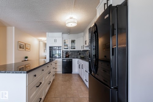 Kitchen featuring white cabinetry, black appliances, dark countertops, a textured tile backsplash, and tile flooring - 807 10011 116 Street, Edmonton, AB 
