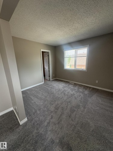Spacious room with new gray carpeting, neutral-toned walls, white trim, and a white-framed window with blinds - 11 Greenfield Estates, St. Albert, AB 