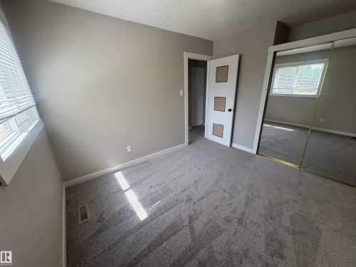 Carpeted room with a window featuring horizontal blinds, a neutral wall color, and a mirrored sliding closet door - 11 Greenfield Estates, St. Albert, AB 
