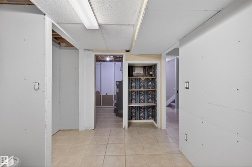 Interior space featuring partial drywall installation, neutral tile flooring, a drop ceiling, a built-in storage niche with shelving, and exposed ceiling joists - 11 Greenfield Estates, St. Albert, AB 