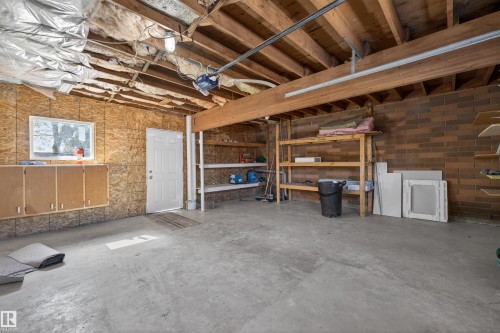Spacious garage featuring a concrete floor, exposed wood ceiling joists, and brick wall - 11 Greenfield Estates, St. Albert, AB 