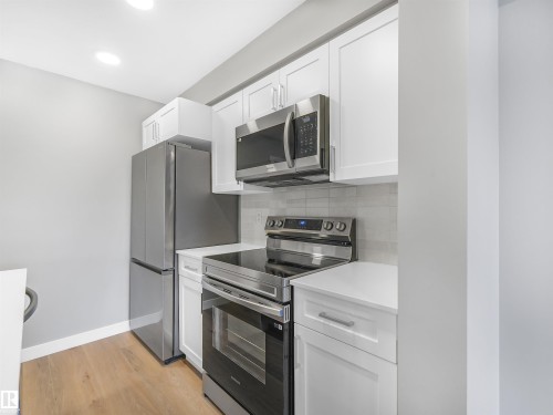 Contemporary kitchen featuring white cabinetry, stainless steel appliances, light countertops, and wood-finish flooring - 318 1506 Tamarack Boulevard, Edmonton, AB 