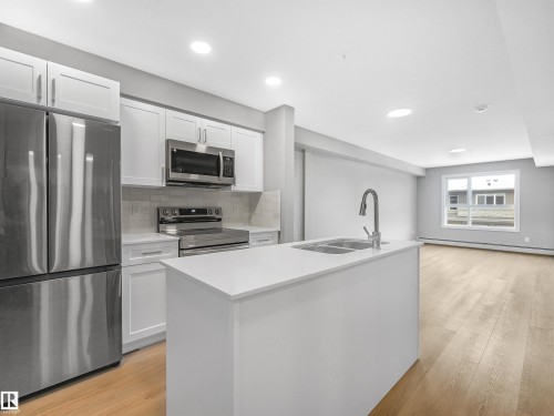 Modern kitchen featuring stainless steel appliances, white cabinetry, a large kitchen island with an undermount double sink, recessed lighting, and wood-finish flooring - 318 1506 Tamarack Boulevard, Edmonton, AB 