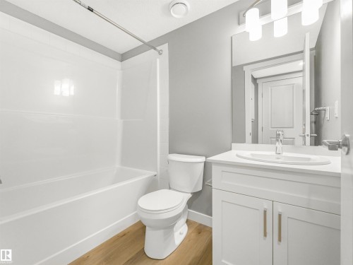 Bathroom featuring a white vanity with an undermount sink, a white bathtub with a shower kit, a toilet, wood-finish flooring, and a mirrored medicine cabinet - 318 1506 Tamarack Boulevard, Edmonton, AB 