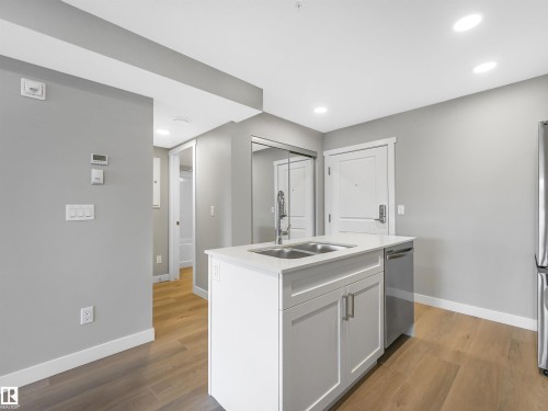 Kitchen island featuring a double-basin stainless steel sink with a gooseneck faucet, white cabinetry, and a white countertop - 318 1506 Tamarack Boulevard, Edmonton, AB 
