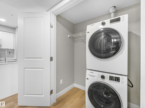 Dedicated laundry closet featuring a stacked washer and dryer, wire shelving, and wood-finish flooring - 318 1506 Tamarack Boulevard, Edmonton, AB 