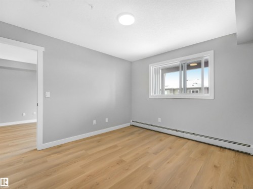 Bright room featuring light wood-finish flooring, a contemporary flush-mount ceiling light, white baseboards, and a sliding window with white trim - 318 1506 Tamarack Boulevard, Edmonton, AB 