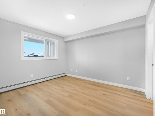 Spacious room featuring light wood-finish flooring, neutral gray wall tones, and white trim - 318 1506 Tamarack Boulevard, Edmonton, AB 