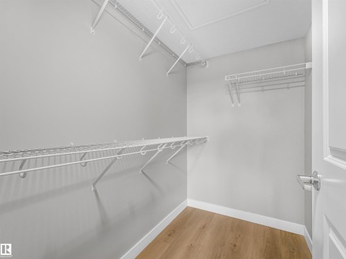 Walk-in closet featuring light wood-finish flooring, white wire shelving, and a bright white door with a polished chrome handle - 318 1506 Tamarack Boulevard, Edmonton, AB 