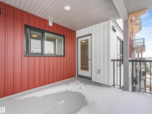 Balcony with red vertical siding, white vertical siding, black-framed window, glass-paneled door, and black metal railings - 318 1506 Tamarack Boulevard, Edmonton, AB 