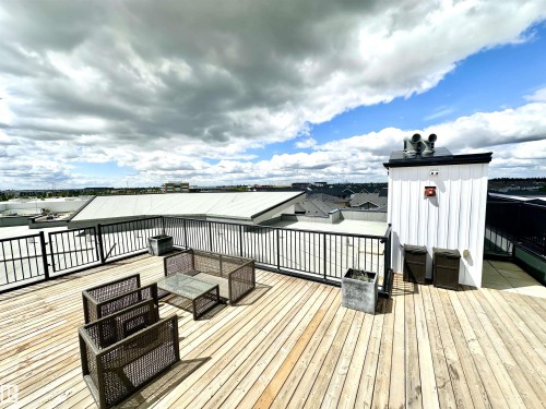 Expansive rooftop deck featuring wood plank flooring, black metal railings, a white shiplap-sided structure, and a concrete planter - 318 1506 Tamarack Boulevard, Edmonton, AB 