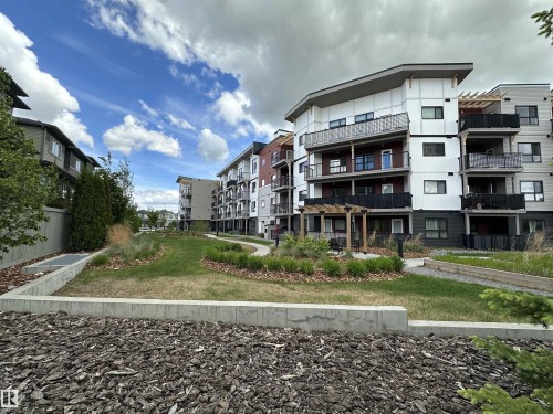 Contemporary apartment building with multi-level balconies and a central landscaped courtyard featuring a walking path, integrated seating, and planted areas - 318 1506 Tamarack Boulevard, Edmonton, AB 