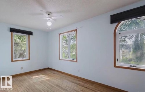 Light-filled room featuring wood-finish flooring, three distinct windows with wood trim, and a ceiling fan with integrated lighting - 10948 75 Avenue, Edmonton, AB 