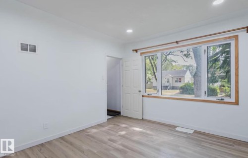 Bright room featuring light wood-finish flooring, recessed ceiling lighting, and a large multi-pane window with wood-trim framing - 10948 75 Avenue, Edmonton, AB 