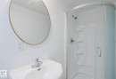 Bathroom featuring a pedestal sink with chrome faucet, a circular mirror with a gold-tone frame, and a curved stand-up shower with integrated shelving - 10948 75 Avenue, Edmonton, AB 