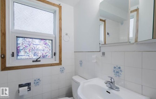Bathroom featuring white ceramic wall tiling with floral accent tiles, a white porcelain sink, and a chrome faucet - 10948 75 Avenue, Edmonton, AB 