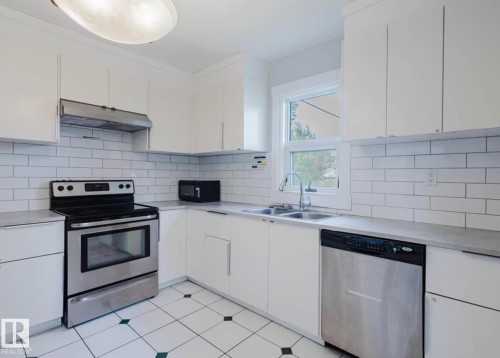 Kitchen featuring white cabinetry, subway tile backsplash, stainless steel appliances, and a double basin sink - 10948 75 Avenue, Edmonton, AB 