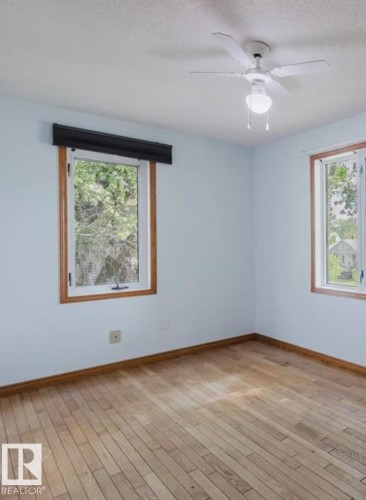 Room featuring wood-finish flooring, two window openings with wood trim, light blue wall paint, and a ceiling fan with integrated lighting - 10948 75 Avenue, Edmonton, AB 