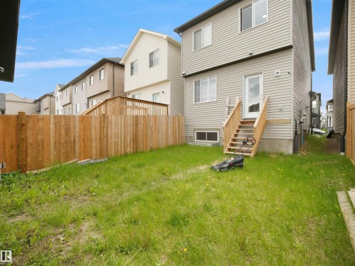 Rear exterior featuring light gray siding, a wood deck with stairs, a glass-paneled door, and a private wooden fence enclosing the yard space - 5022 Kinney Link Sw, Edmonton, AB 