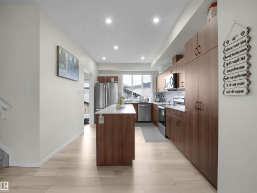 Modern kitchen featuring light wood-finish flooring, recessed ceiling lighting, a center island with a light-toned countertop, and brown wood-finish cabinetry - 5022 Kinney Link Sw, Edmonton, AB 