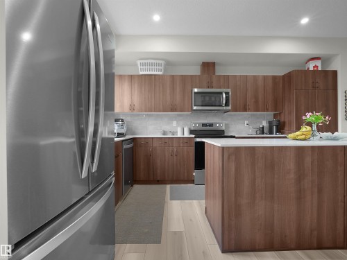 Kitchen featuring a large stainless steel refrigerator, wood-finish cabinetry, white countertops, tile backsplash, and an integrated kitchen island - 5022 Kinney Link Sw, Edmonton, AB 