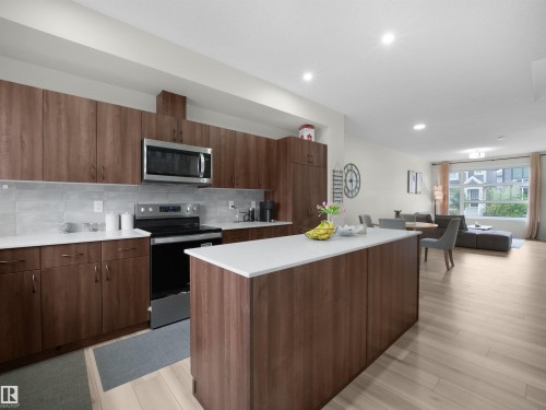 Kitchen featuring wood-finish cabinetry, stainless steel appliances, light-toned countertops, and a gray tile backsplash - 5022 Kinney Link Sw, Edmonton, AB 