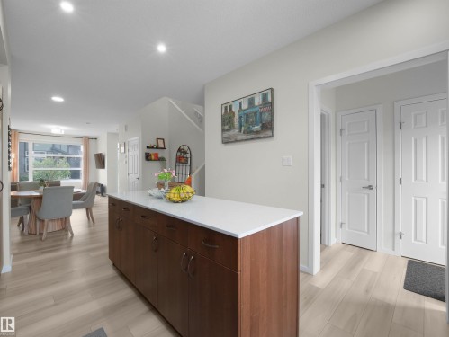 Open-concept living space featuring a central island with rich wood-finish cabinetry and a light-toned countertop - 5022 Kinney Link Sw, Edmonton, AB 
