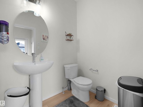 Pedestal sink with chrome faucet, circular mirror, and light wood-finish flooring - 5022 Kinney Link Sw, Edmonton, AB 