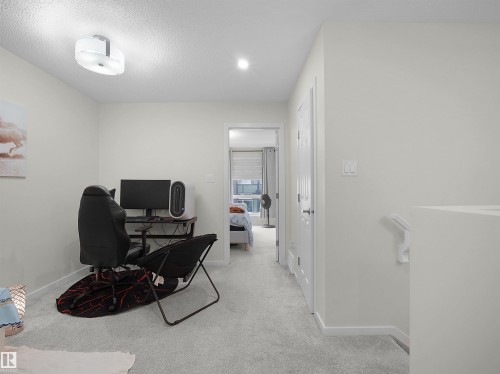 Versatile open landing space featuring light gray carpeting, neutral wall finishes, a modern flush-mount ceiling light fixture, and white trim - 5022 Kinney Link Sw, Edmonton, AB 