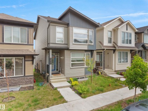 Contemporary two-story residence featuring a multi-toned facade with vertical and horizontal siding accents, a prominent front entry with a blue door, a covered porch, and white-framed windows - 5022 Kinney Link Sw, Edmonton, AB 