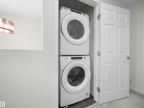 Full-size stackable washer and dryer unit within a dedicated closet, featuring a paneled interior door and soft gray carpeting - 5022 Kinney Link Sw, Edmonton, AB 