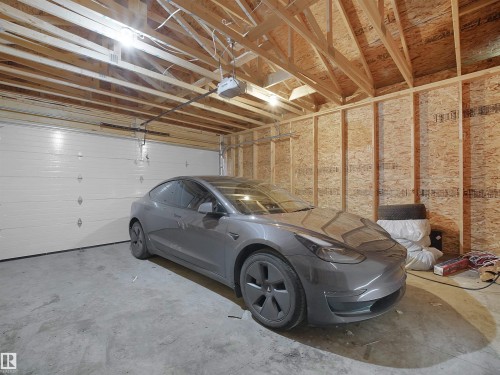 Spacious garage featuring a concrete floor, exposed wood framing, and an automatic overhead door - 5022 Kinney Link Sw, Edmonton, AB 