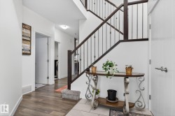 Foyer featuring wood-finish flooring, white walls, and a staircase with dark wood newel posts and metal spindles - 