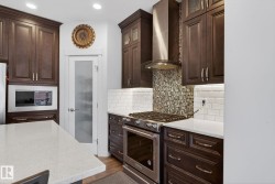 Kitchen featuring dark wood cabinetry, white quartz countertops, subway tile backsplash, stainless steel appliances, and a frosted glass pantry door - 