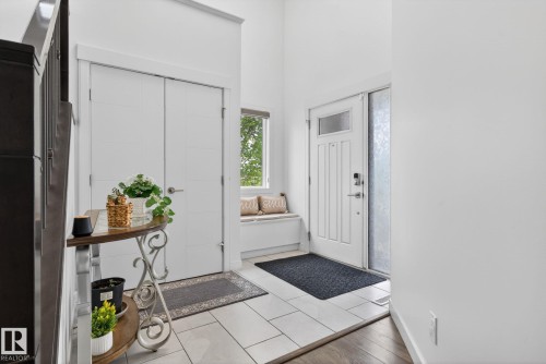 Bright entryway featuring large format tile flooring, a built-in window bench, a full-lite entry door with frosted glass sidelight, and a closet with bifold doors - 704 39 Street, Edmonton, AB 