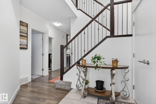Foyer featuring a dark wood-finish staircase with wrought iron balusters, light wood-finish flooring, and white interior doors with contemporary hardware - 704 39 Street, Edmonton, AB 