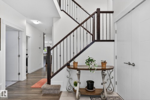 Entryway featuring a dark wood staircase with wrought iron balusters, white paneled doors, wood-finish flooring, and a flush mount ceiling light - 704 39 Street, Edmonton, AB 