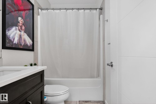 Bathroom featuring a white tub and shower combination, dark wood-finish vanity with a white countertop, and light-toned tile flooring - 704 39 Street, Edmonton, AB 