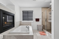 Integrated fireplace with a tile surround, a built-in soaking tub with deck-mounted fixtures, a glass-enclosed shower, and large format floor tiling - 