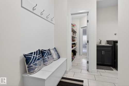 Entryway featuring a built-in bench with storage, wall-mounted coat hooks, and light-toned rectangular floor tiles - 704 39 Street, Edmonton, AB 
