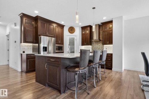 Spacious kitchen featuring an island with seating, dark wood cabinetry, stainless steel appliances, a tile backsplash, and wood-finish flooring - 704 39 Street, Edmonton, AB 
