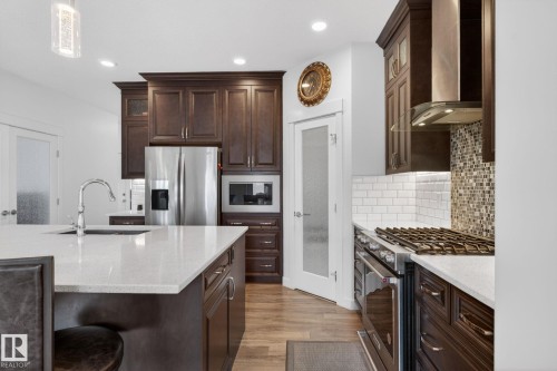 Kitchen featuring dark wood cabinetry, white countertops, stainless steel appliances, and wood-finish flooring - 704 39 Street, Edmonton, AB 