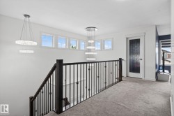 Upper-level landing featuring a dark wood and wrought iron staircase railing, multiple transom windows, and two tiered crystal chandeliers - 