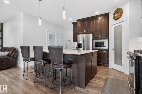 Kitchen featuring a central island with countertop seating, dark wood cabinetry, stainless steel appliances, and wood-finish flooring - 704 39 Street, Edmonton, AB 