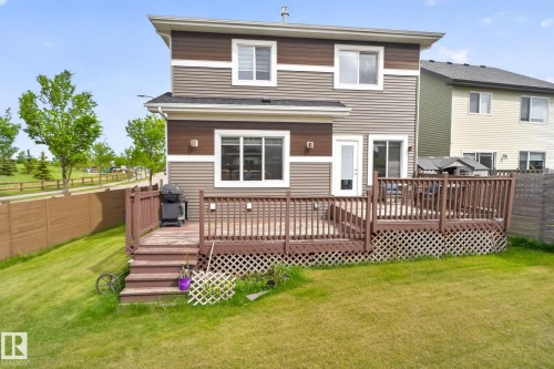 Two-story exterior featuring brown and gray siding, multiple windows with white trim, a sliding glass door, and a full-light entry door accessing a multi-level wooden deck - 704 39 Street, Edmonton, AB 
