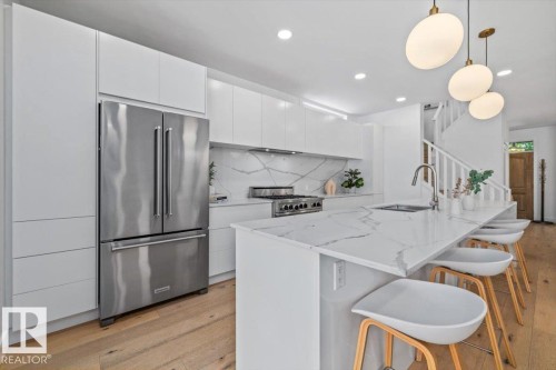 Contemporary kitchen featuring an expansive island with white countertop, integrated sink, and seating for four - 10641 126 Street, Edmonton, AB 