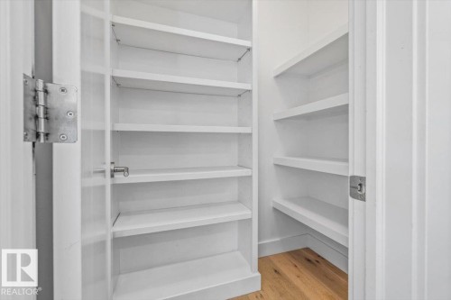 Pantry with extensive white shelving, wood-finish flooring, and a white door with a metal latch - 10641 126 Street, Edmonton, AB 