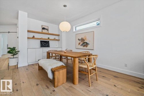 Dining area featuring wide plank wood-finish flooring, a linear transom window, and a modern spherical pendant light - 10641 126 Street, Edmonton, AB 