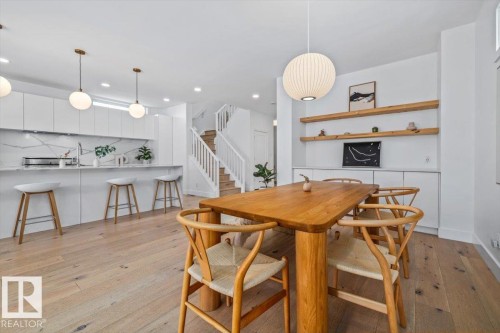 Open-concept living space featuring light wood-finish flooring, white walls, and a modern kitchen with a waterfall island - 10641 126 Street, Edmonton, AB 